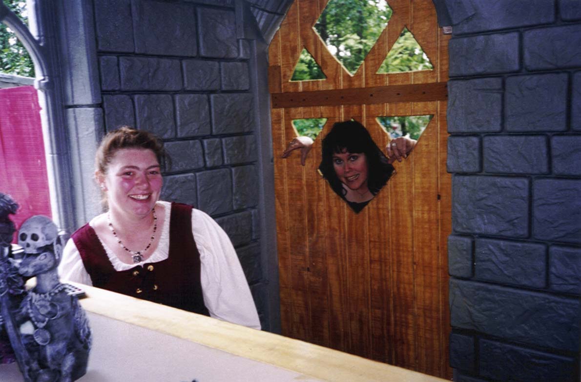 A Xena-esque Peg sticks her head & hands through windows in the shop door while Maddy grins evilly.