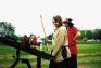 Mo grinning as he points his steel-tipped arrow shooting ballista at a target.